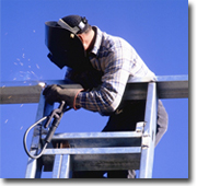 Photo of a man standing on a ladder welding a steel frame.