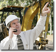 Photo of a builder standing in front of a bulldozer talking on his mobile phone.