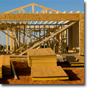 Photo of a timber house frame with timber panels stacked in front of the house.