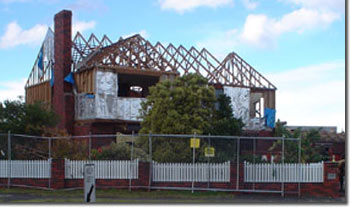 Photo of a two-storey house. The framework of the roof is exposed and the site is fenced off. 