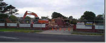 Photo of a fenced off site with an excavator clearing the debris. 