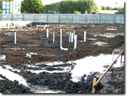 Photo of a cleared site with puddles around the area. There are some markers and pipes on the site. 