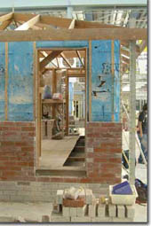 Photo of a brick veneer house under construction. Some of the frame, the sarking and a partly completed brick wall are displayed. 