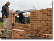 Photo of a bricklayer placing a lintel over an opening in a brick wall.