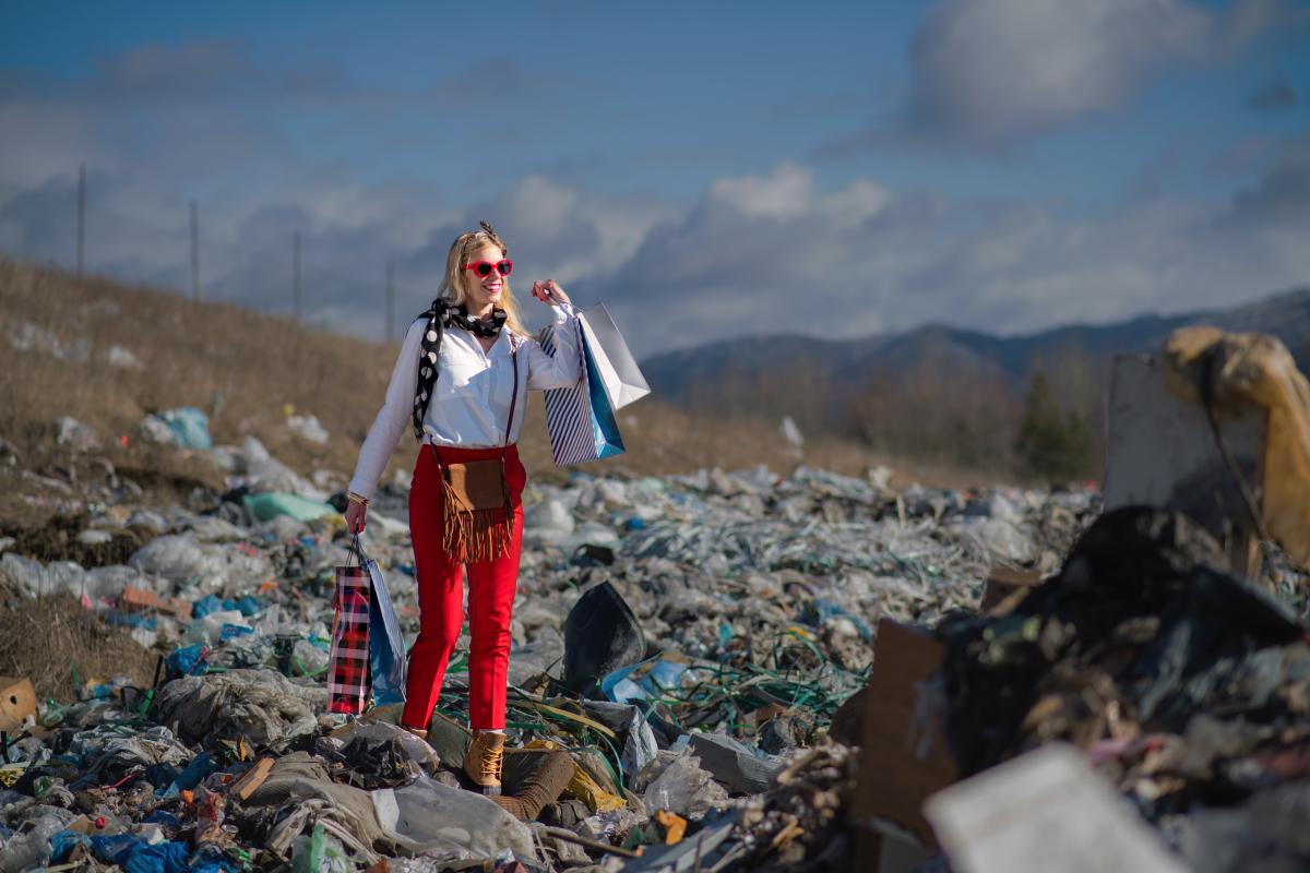 Woman with shopping bags standing in the middle of a garbage dump