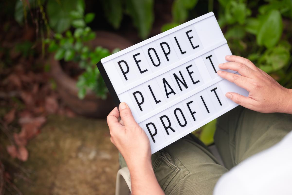 Person holding a lightboard with the words; people, planet, and profit